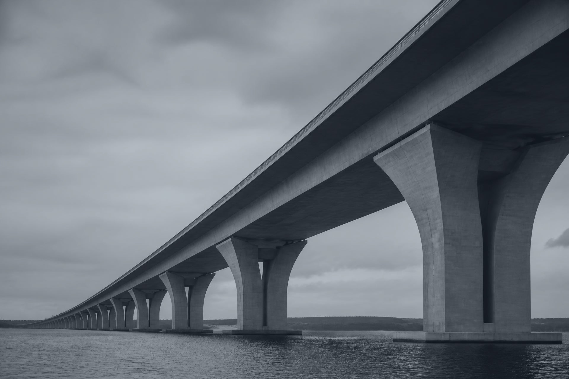 A long concrete viaduct extending across calm water under an overcast sky